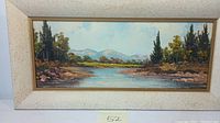 Front view of framed oil painting showing flowing river landscape with trees and mountains.