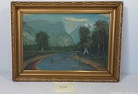 Frontal image of the signed oil on canvas painting showing the river landscape with mountains, trees, and a small boat, in an ornate gold frame.