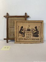 Front view of the antique embroidery featuring two seated figures at a table with the quote 'Give Us This Day Our Daily Bread'.