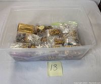 Plastic container holding multiple bags of jewelry charms, chains, beads mostly gold and silver-tone metal parts