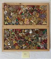 Wooden trays filled with various holiday themed costume jewelry items including brooches, earrings, and necklaces. Numerous colorful pieces with Christmas motifs such as Santa hats, snowflakes, candy canes, and poinsettias.