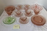 Overall view of the pink glass cups, saucers, salad plates, trays, and candle holders with green relish tray, arranged on a white surface.