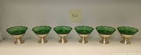 Six vintage dessert cups with emerald green scalloped glass bowls and aluminum pedestal bases lined up in a row