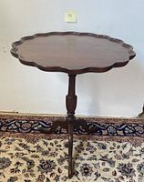 Front view of vintage wooden pie crust scalloped edge tilt top table standing upright on Queen Anne legs on patterned rug.