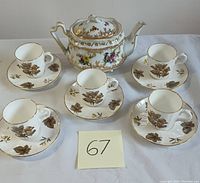 Full tea set displayed, includes teapot and five demitasse cup and saucer sets with brown leaf patterns on cups and saucers.