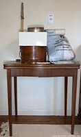 Antique wooden folding table with several boxes and bags on top, including a tape measure, a white box, hatboxes and a paper bag.