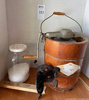 Full view of antique White Mountain French ice cream maker with wooden bucket and metal crank, jug of rock salt labeled not for consumption, and vintage iron apple peeler with wooden handle.