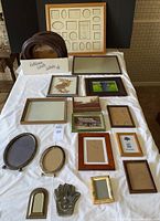 Assorted frames displayed on white sheet, shows variety of sizes, materials, and styles including oval and rectangular frames, pressed flower art, Hamsa hand metal piece, and small brass mirror.