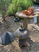 Photo showing the birdbath, angel statue on top, stone pagoda sculpture, Squirrel Buster bird feeder hanging nearby, and black dome-shaped squirrel guard on ground.