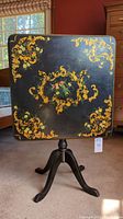 Square black table top flipped vertical showing gold scrollwork and floral centerpiece