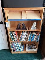 Front view of wooden bookcase filled with assorted books and three bookends on the middle shelf.