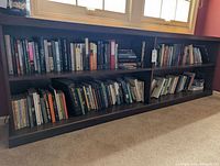 Bookshelves with a wide range of hardcover and trade paperback books, mostly fiction, organized on three shelves.