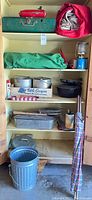 Cabinet with red cooler box, blue gas lantern, enamel cups and plate, cast iron cookware, several pots, assorted utensils, wind/privacy screen folded, metal bucket and pan