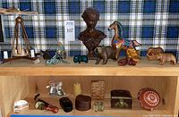 Wide view of two wooden shelves with various carved and collectible items arranged, showing multiple animal figurines, boxes, a carved bust, and more.