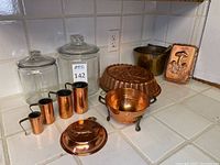 Overview of all items together showing copper molds, colander, measuring cups, brass bucket with scoop, and glass canisters.