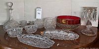 Wide view of assorted clear and red cut glass pieces including decanter, bowls, candy dish, serving dishes, and vase.