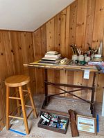 Overall view of drafting table, wooden stool, tool box and tabletop supplies