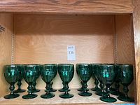 Set of 16 green glass stemware goblets arranged on a wooden shelf.