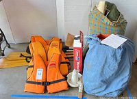 Overview of three orange Helmsman PFDs, wooden paddles, small white anchor, Coleman box and denim storage bag