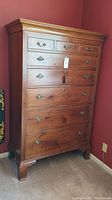Full frontal view of the tall highboy dresser showing 8 drawers, brass pulls, and crown molding top.