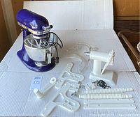 KitchenAid cobalt blue tilt-head stand mixer with multiple white attachments and a white crank meat tenderizer laid out on a white surface