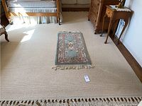 Wide shot of large cream rug and small blue-green floral accent rug on floor beside furniture