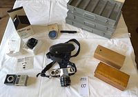 Full view of camera, lenses in boxes, slide holders, metal storage trays, and accessories on white cloth