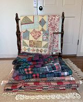 Full view of antique wooden quilt rack with three quilts folded and draped over it on a hardwood floor in front of a door.
