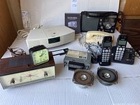 Wide shot of all radios, phones, clocks, and speakers included in the lot.