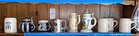 Overview of all nine steins on a blue shelf including various ceramic designs and one pewter stein