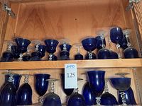 Shelf full of assorted blue goblets with clear stems in a wooden cabinet.