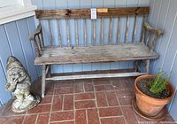 Full view of the lot including the weathered wooden bench, cement garden gnome statue, and terra-cotta pot with plant positioned on a red tiled porch floor against a light blue wall.