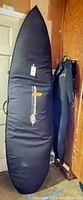 Surfboard in black Destination Surf carry case upright beside hung wetsuit