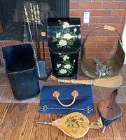 Photo showing entire set with tole painted holder, metal wood holder, brass wood holder with pine cones, fireplace tools, bellows, broom, and canvas sling.