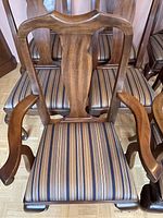 Close-up of armchair seat showing striped upholstery and carved mahogany frame.
