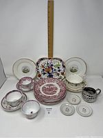 Full set of assorted antique porcelain including plates, cups, saucers, butter pats, creamer, and cake server arranged before a ruler for scale
