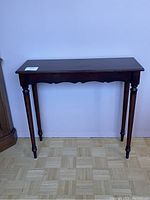 Front view of the Bombay Company mahogany finish hall table with turned legs and scalloped apron.