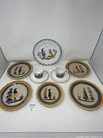 Seven items displayed: five hand-painted Henriot Quimper plates showing country figures and two Villeroy & Boch cups and saucers with hand-painted scenery
