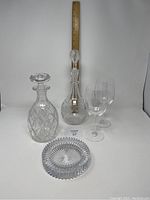 Front view showing diamond-cut pattern decanter, taller etched decanter with stopper, two etched wine glasses, and ridged crystal ashtray on white background with ruler for size reference.