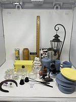 Photo showing various decorative items arranged including ceramic vases, a small wooden chest, candle holders, abstract stone carving, glass votives, a black candle snuffer, and blue ceramic containers.