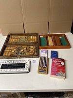 Top-down view of backgammon set opened with pieces and dice inside, cribbage board case, card holder, cards and Scrabble dictionary on a table
