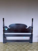 Front view of full mahogany headboard showcasing wide, curved center panel and tall carved posts with finials.