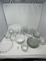 Wide shot showing entire lot of kitchenware including vintage Pyrex bowl, various glass bowls, plates, and glasses.