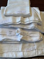 Stack of white linen tablecloths showing size tags and some evidence of repairs