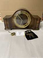 Full view of Mauthe walnut mantle clock showing clock face, pendulum, two winding keys, and black pouch for accessories.