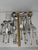 Flatware arranged on white surface showing various silver plated serving pieces with a ruler for scale.