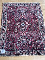 Full view of the rectangular red oriental rug showing detailed floral pattern and cream border on wooden floor.
