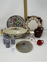 Front view of entire lot showing centerpiece bowl, decorative plates, condiment set, pottery jugs and candleholders
