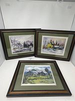 Three framed prints showing rural and architectural scenes arranged on a white surface.