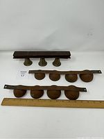 Photo showing one set of three brass bells mounted on a wooden bar and two sets of rusted metal sleigh bells mounted on long strips with a ruler for scale.